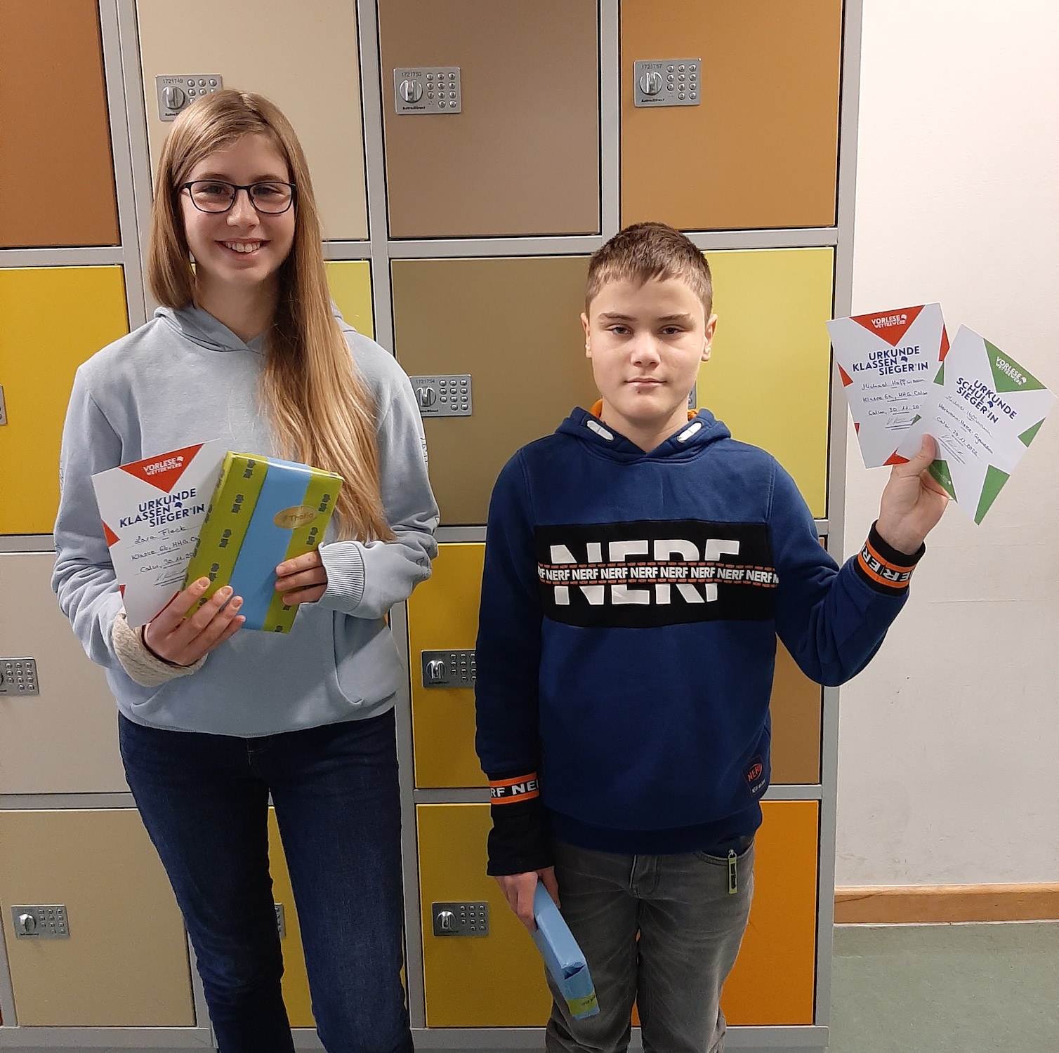 Eine Schülerin und ein Schüler halten Flyer und ein Buch 